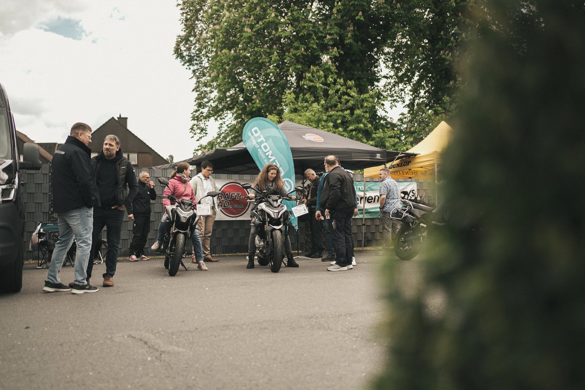 Besucher informieren sich an verschiedenen Ständen mit ausgestellten Motorrädern auf dem Außengelände.