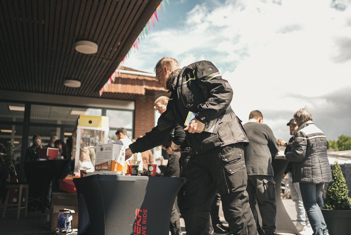 Besucher bedienen sich an einem Stehtisch mit Getränken und Snacks vor dem Modeka-Gebäude.