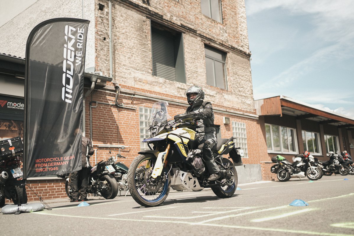 Motorradfahrer fährt auf einer Suzuki durch einen markierten Parcours vor dem Modeka-Gebäude.