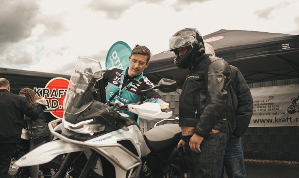 Zwei Personen betrachten gemeinsam ein CF Moto Motorrad auf einem Veranstaltungsgelände.