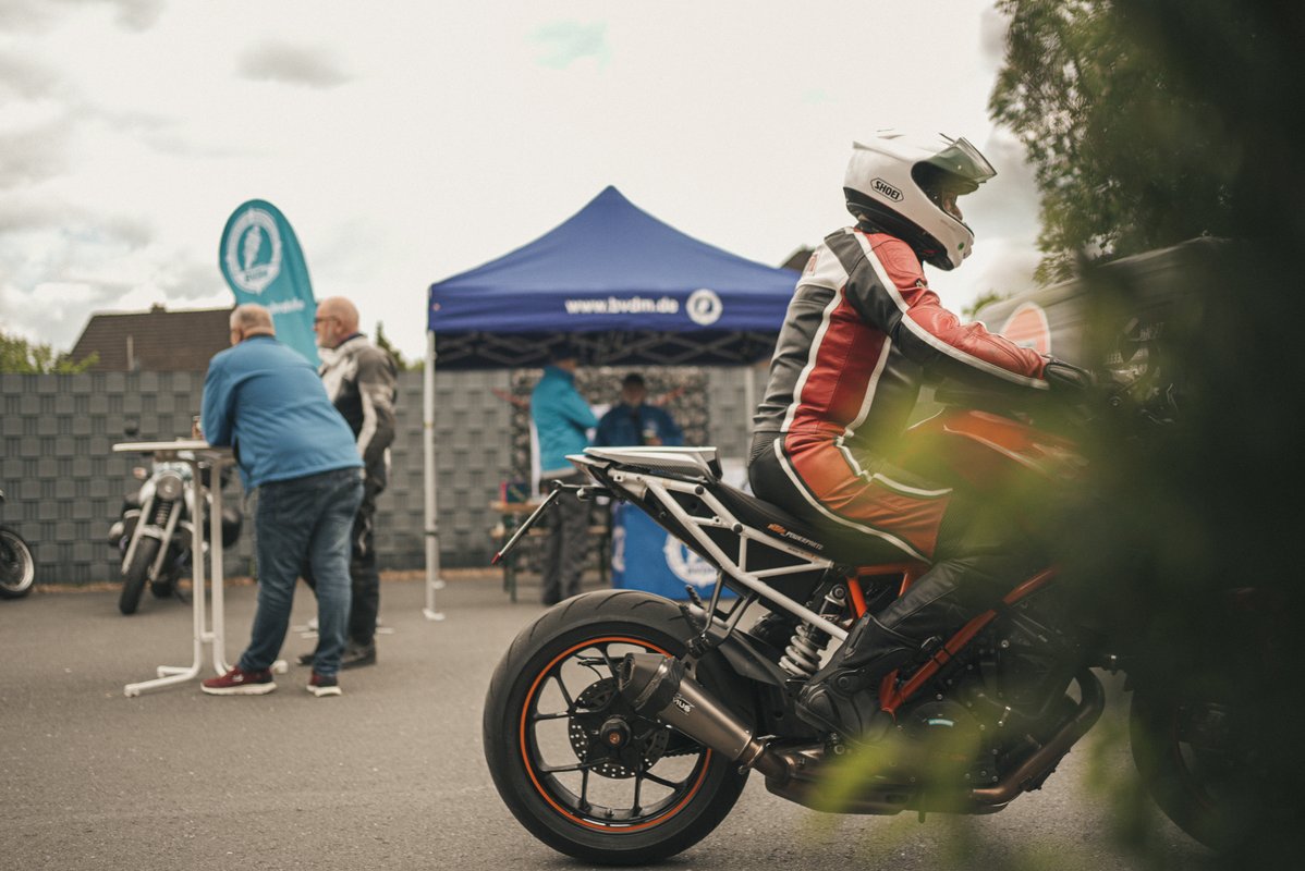 Motorradfahrer in rot-weißer Schutzkleidung sitzt auf einem Sportmotorrad auf dem Eventgelände.